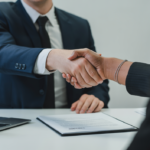 Professional lawyer and tech founder shaking hands across a clean desk with a laptop and blank contract pages, symbolizing SaaS contract agreement and legal partnership.